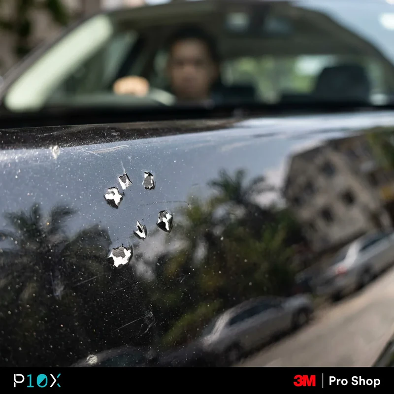 Close-up shot of a dark-colored car's bonnet, subtly revealing small stone chip damage on its paint surface while driving on a busy Kuala Lumpur highway.