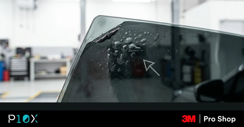 Technician inspecting tint on a Proton X50 side window inside an automotive workshop.