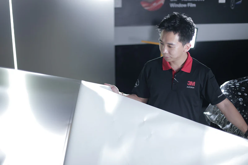 A 3M technician handling a window-film sheet before installation.