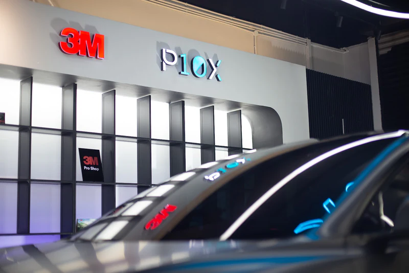 Tinted windscreen inside a workshop with 3M signage reflected in the glass.