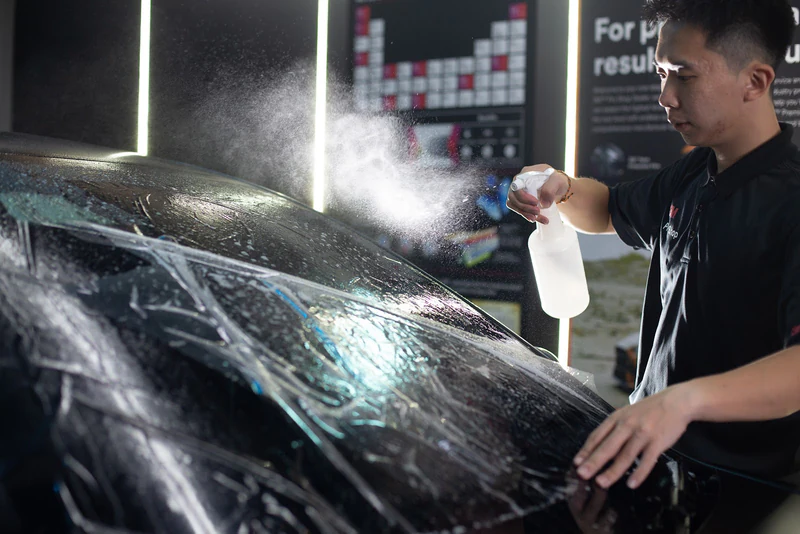 A technician sprays installation solution on windscreen glass before tint fitting.