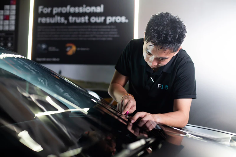 Technician squeegeeing 3M window film across a windscreen during a professional window tint installation.