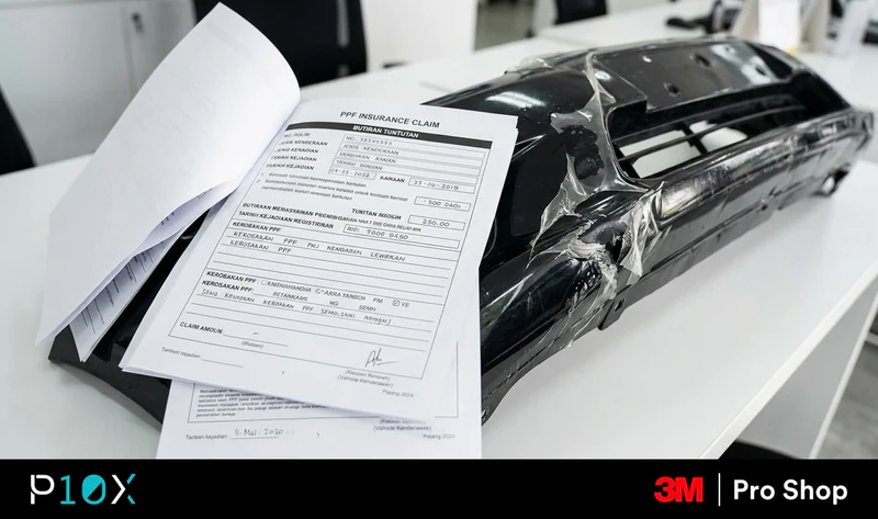 PPF insurance claim Malaysia documentation pack on a clean white desk beside a damaged front bumper with paint protection film peeling at the impact point.